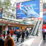 Besucher im Foyer der EuroShop in der Messe Düsseldorf mit Willkommensscreen und Themenübersicht